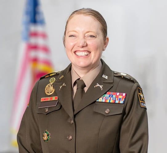 Headshot of a person in a military uniform sitting in front of an American Flag.