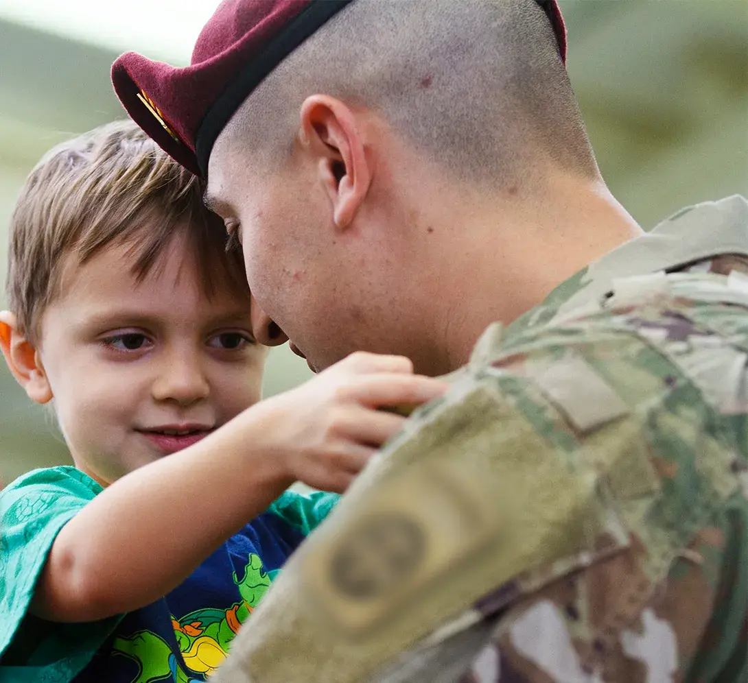An adult in military inform embracing a younger child in a hug