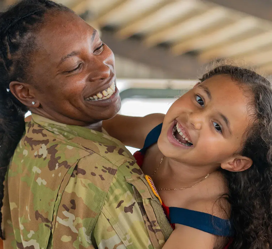 An adult in military inform embracing a younger child in a hug.