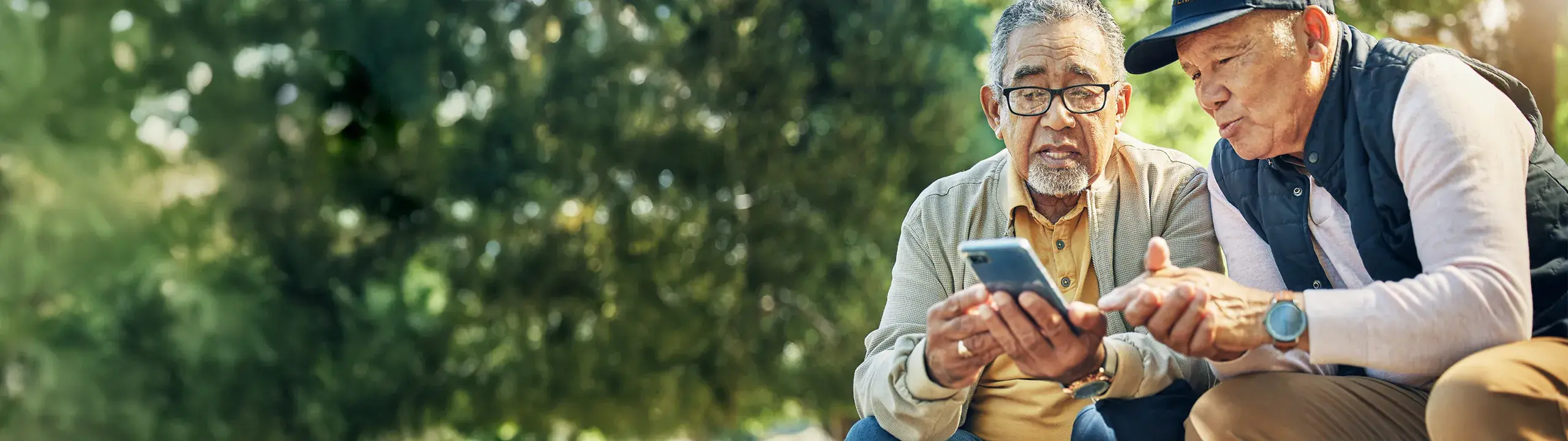 Image of two people sitting in a park using a phone.