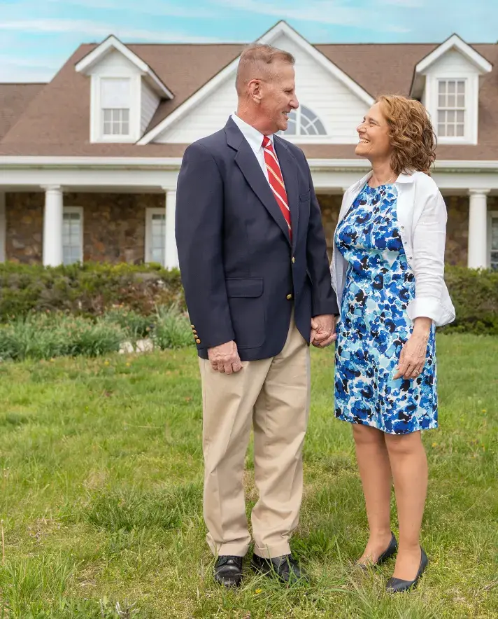 Two people in formal attire standing on the grass in front of a house.
