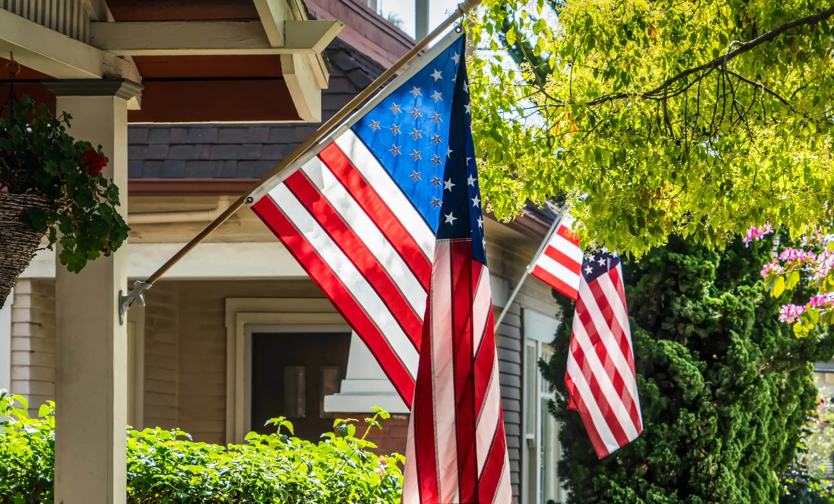 Two American flags hanging from the porches of two houses. 