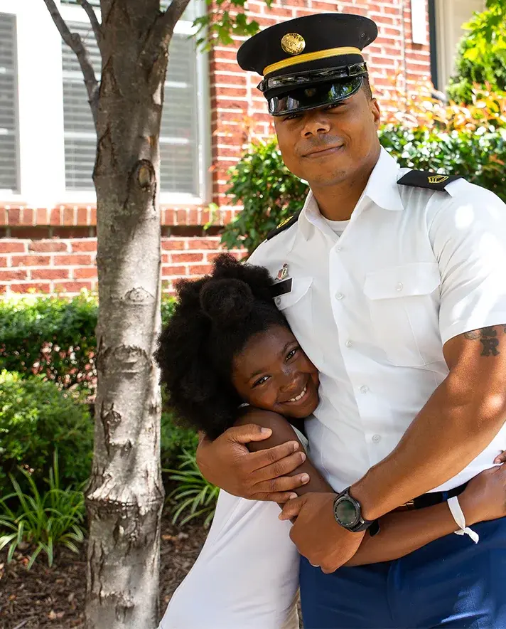 A man in a military uniform hugging a small child. 