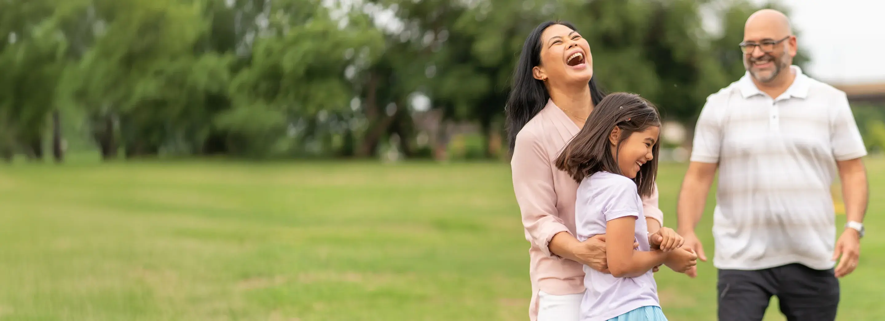 Two adults and one child laughing together in a field.