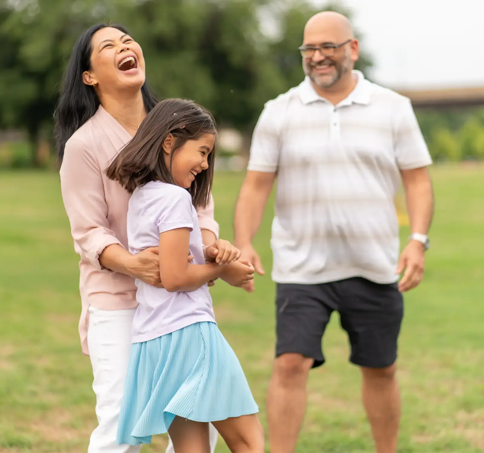 Two adults and one child laughing together in a field.