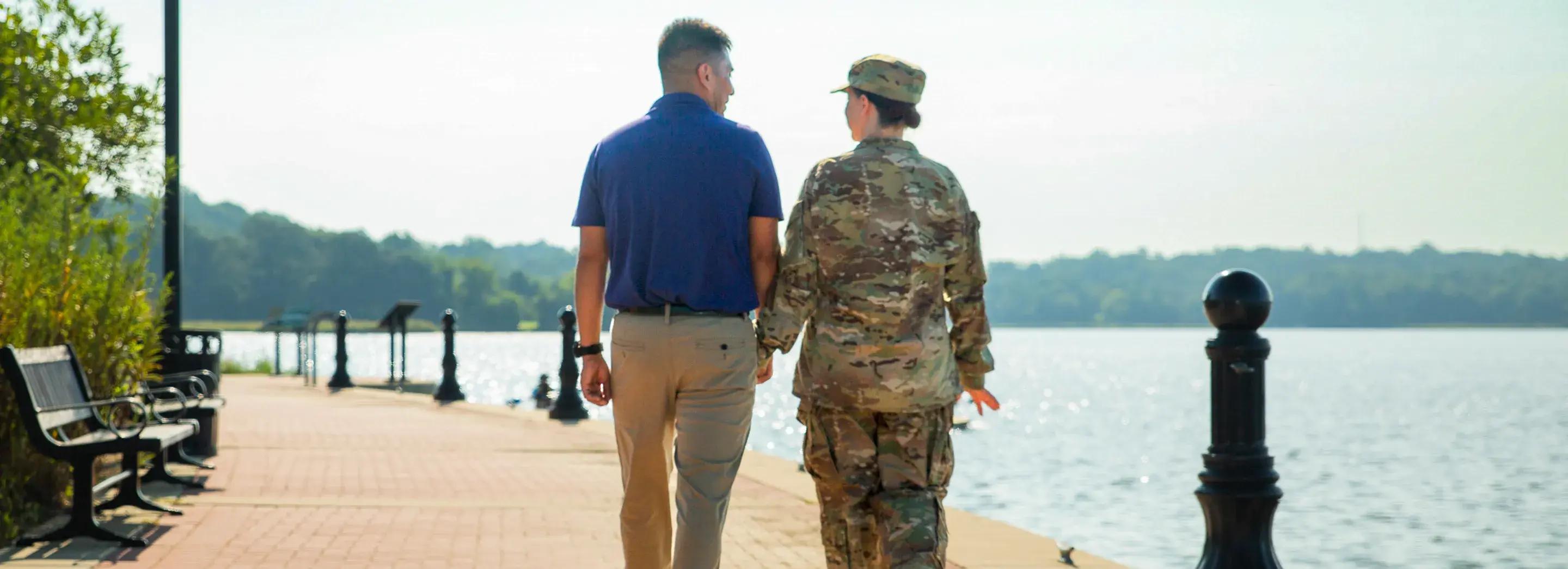 Two people holding hands while walking on a boardwalk. One is wearing a military uniform.