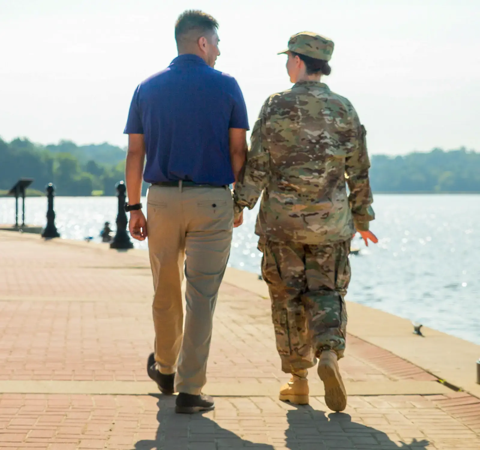 Two people holding hands while walking on a boardwalk. One is wearing a military uniform.