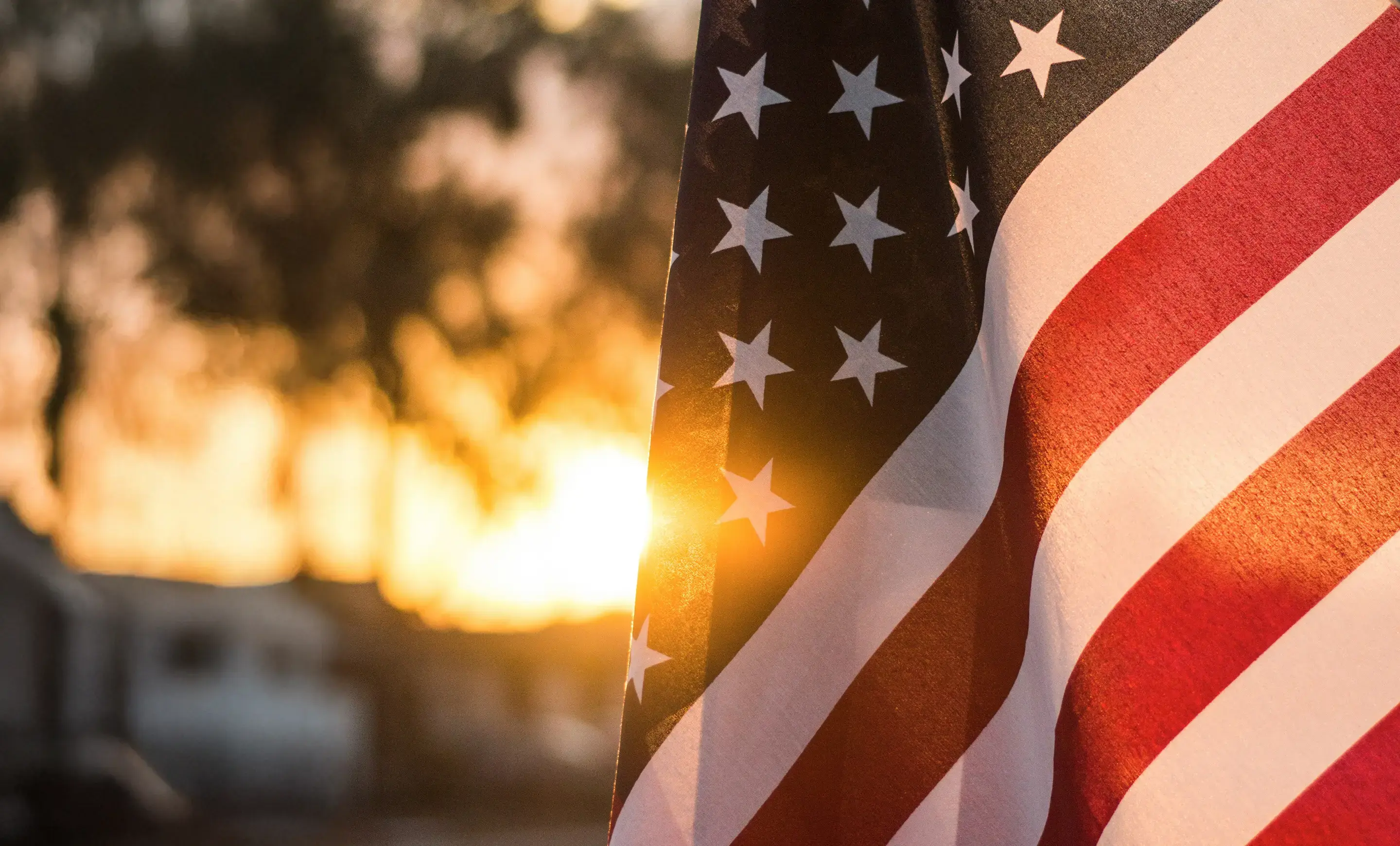 Image of an American Flag with a sunset in the background.